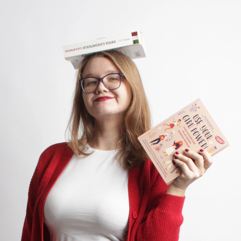 Online Italian teacher Viktoria Laskina, smiling while balancing an Italian coursebook on her head.